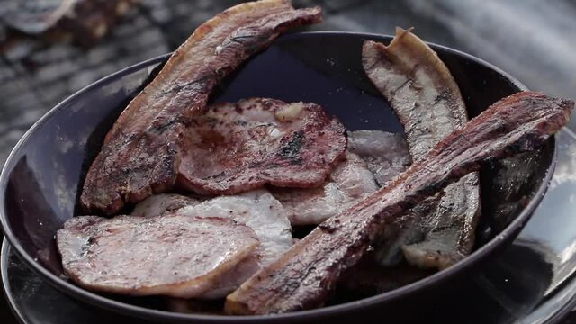 Una mano de un chico sacando panceta de la parrilla a un plato.