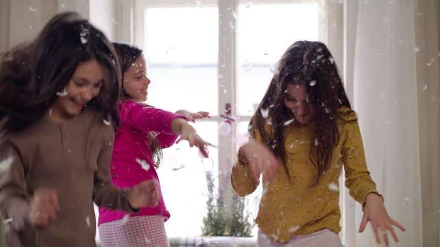 Group of small girl friends on kids sleepover slumber party, throwing feathers.