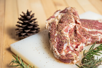 Piece of raw pork steak on a plastic plate with rosemary, olive oil and black pepper close up with copy space.