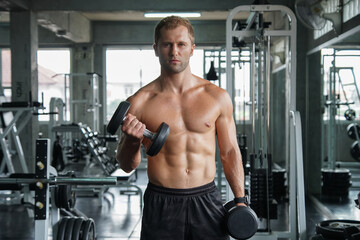 Fototapeta na wymiar Young handsome muscular man working out with dumbbells. Strong bodybuilder in the gym fitness