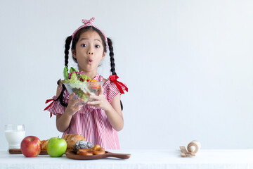 Cute Asian girl with surprise face holding a vegetable salad bowl for breakfast, white background