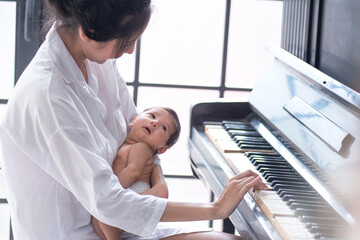 Asian mother and cute baby playing old piano, a good time with a newborn baby