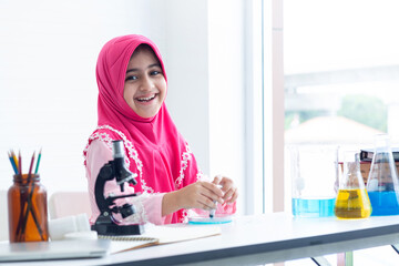 Cute Muslim girl wear hijab enjoys learning science, looking at camera with joyful