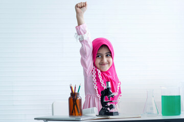Cute Muslim girl wear hijab enjoys learning science, Held a fist above her head