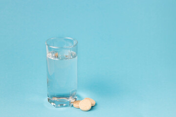 Glass of water and pills on a blue background close-up. Vitamins. Copy space.