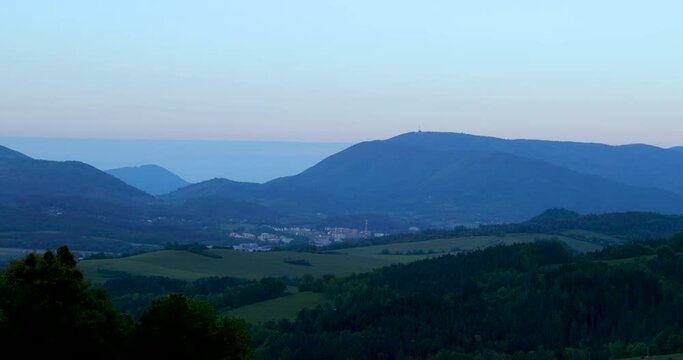 View of Radhost surrounding the hills and forests and the town of Zubř&iacute; lying along the Beskydy hills during the early evening when the sun has set and the landscape lies in the shade.
