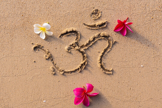 The sound "Om" or "AUM" written in Sanskrit - in the Hindu and Vedic traditions - sacred sound, the original mantra. Used in yoga practices and meditation techniques. Frangipani flowers on the sand