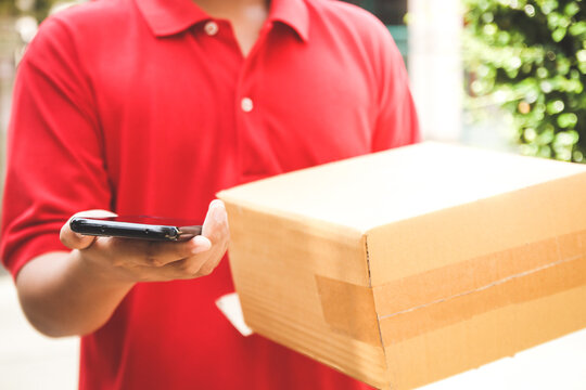 The delivery staff wears red shirts, carrying brown paper boxes and smartphones. Stand in front of the client's house. Online shopping business concept, social distance. New Normal