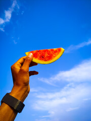 A hand hold a piece of watermelon isolate on blue sky background.