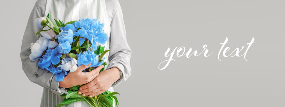 Female florist with beautiful bouquet of peonies on grey background with space for text