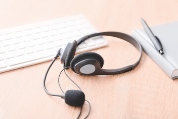 Headset, notebook and PC keyboard on table of technical support agent in office
