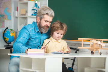 Obraz premium Cute child boy with teacher in classroom near blackboard desk. Pupil of primary school study indoors. Home school for pupil.