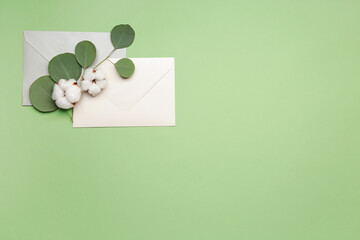 Beautiful cotton flowers, envelopes and eucalyptus leaves on color background
