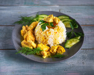 Homemade food on a gray round plate. Rice and chicken meat with vegetables and herbs on a wooden tray of blue color
