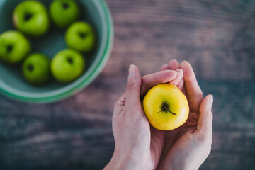 plant-based food, bowl of green apples and hand holding a smaller yellow one next to it