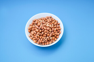 A bowl of peanuts or ground nuts on a blue background.  Food and drinks concept 