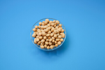 A bowl of peanuts or ground nuts on a blue background.  Food and drinks concept 