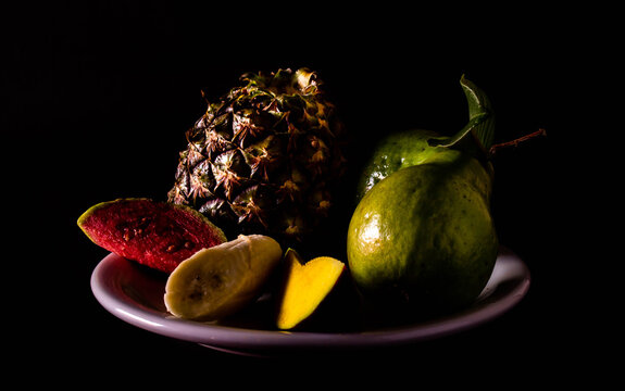 whole and cut varied fruits on a plate. Neutral black background with pictorial lighting. Vegetarian or vegan breakfast concept. © Horacio Selva