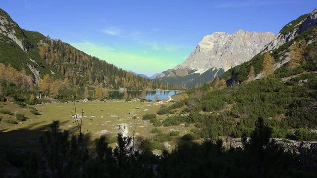 View of tourists walking toward Seebensee, an amazing lake high in the mountains of the alps in autumn with the peak of Zugspitze in the background. Austria