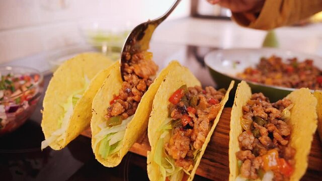 Woman hand stuffing hard taco shells - adding the ground meat and vegetables filling, camera orbit, close up, slow motion. Phases of making tacos.