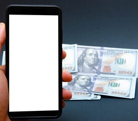 Dollars and smartphone. A male hand holds a smartphone on the left, in the background dollar bills are on a black background