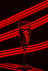 A glass of champagne on a black background with the effect of drawing red light on a long shutter speed. Concept idea for decorating a party or holiday with a neon effect