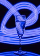 A glass of champagne on a black background with the effect of drawing blue light on a long shutter speed. Concept idea for decorating a party or holiday with a neon effect