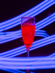 red-lit champagne glass on a black background with the effect of drawing blue light on a long shutter speed. Concept idea for decorating a party or holiday in neon style