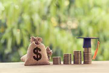 Black graduation cap, Hat and US dollar bag on rows of rising coins, on a table. Education funding, financial concept. Depicts savings for child knowledge for future studies.