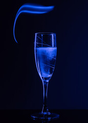 A glass of champagne on a black background with the effect of drawing blue light on a long shutter speed. Concept idea for decorating a party or holiday in neon style.