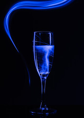 A glass of champagne on a black background with the effect of drawing blue light on a long shutter speed. Concept idea for decorating a party or holiday in neon style.