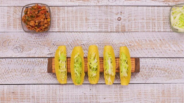 Making delicious hard shell tacos - with the filling ingredients in bowls marching through the screen and assembling the popular dish - top view, stop motion animation
