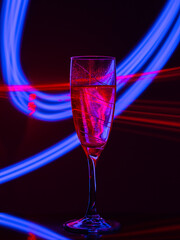red-lit champagne glass on a black background with the effect of drawing blue light on a long shutter speed. Concept idea for decorating a party or holiday in neon style