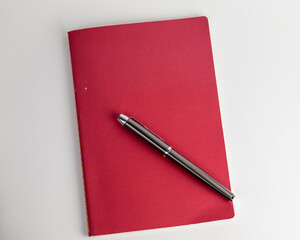 Klasyczne pióro atramentowe na czerwonym zeszycie na białym tle