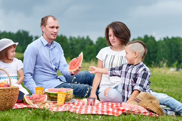 Happy family eating watermelon at a picnic. Picnic in the meadow or park. Young friends and their children in nature