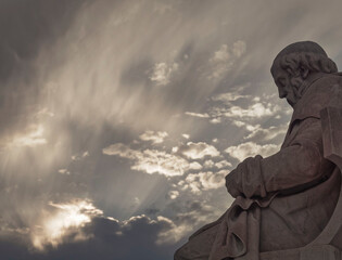 Plato tstue the ancient Greek philosopher, under impressive cloudy sky with sun patches