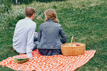 Young couple in love on picnic sitting on tablecloth in red cell. Love couple resting in nature in...