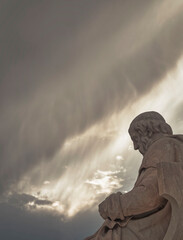 Plato tstue the ancient Greek philosopher, under impressive cloudy sky with sun patches