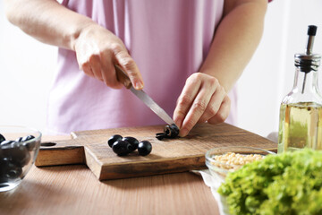Woman cuts black olives. The process of making salad