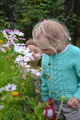 Happy caucasian children sisters walk in nature outdoor in summer lifestyle. Little girls enjoy the smell of flowers daisies