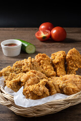 Crispy fried chicken in wicker basket serve with cucumber, tomato and ketchup on wooden background.