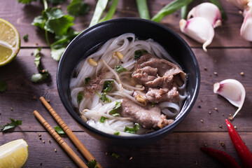 Asian cuisine, Vietnamese pho bo soup in a black plate on a wooden background