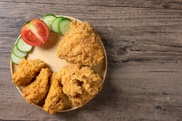 Crispy fried chicken on Round Wood plate served with cucumber, tomato and ketchup on wooden background. top view. Flat lay with copy space.