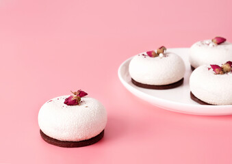 Mousse pastry dessert covered with white chocolate and decorated with rose buds on pastel pink background. Modern stylish cake. Copy space. Close-up.