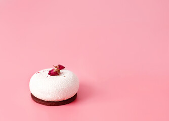 One mousse pastry dessert covered with white chocolate and decorated with rose buds on pastel pink background. Modern stylish cake. Flat lay style. Copy space. Close-up.