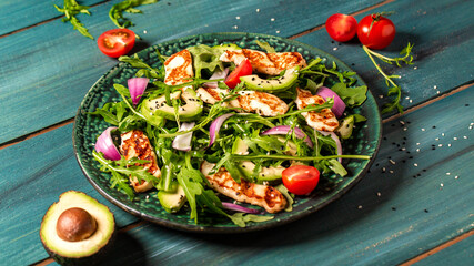 Fresh salad plate with arugula, halloumi cheese, tomatoes and avocado wooden background close up. Healthy food. Green meal