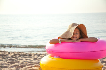 Tan girl wearing straw hat and yellow swimsuit relax on the beach and take sunbath on summer...