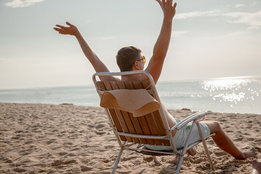 The man resting on the deck chair on the sandy beach