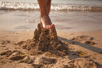 The man legs damaged the wet sandy castle
