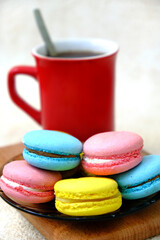 Colorful french Sweet Pastries Macaroons on glass table and red coffee mug on wooden tray.